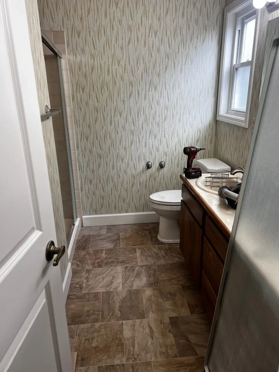 Outdated bathroom before remodel in Boise, Idaho, with dated wallpaper and worn flooring